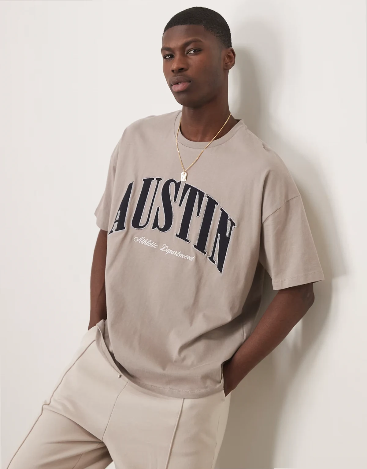 – Brązowy T-shirt oversize z obniżoną linią ramion i aplikacją na piersi